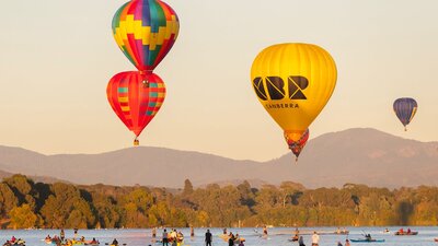 Four floating hot air balloons over lake in Canberra