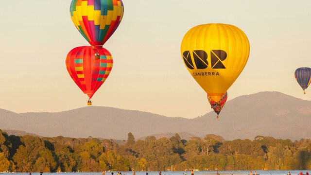 Four floating hot air balloons over lake in Canberra