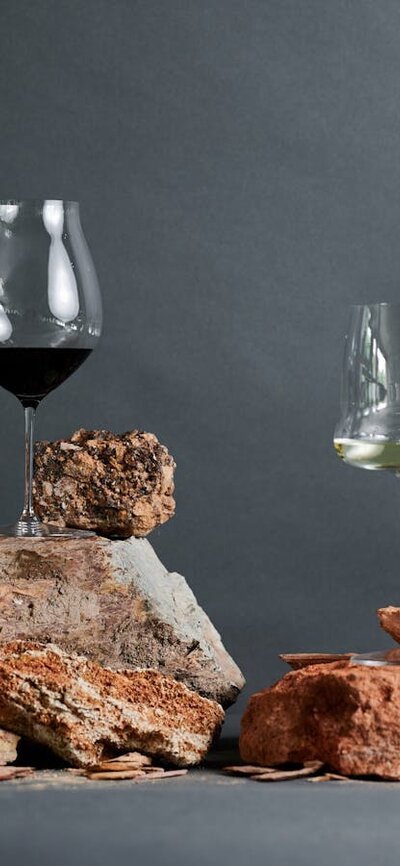 Glasses of wine are balanced on top of red clay soils in a studio shot.