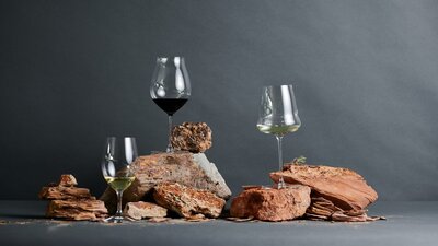 Glasses of wine are balanced on top of red clay soils in a studio shot.