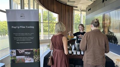 Two people chatting to a vitner over bottles of wine.