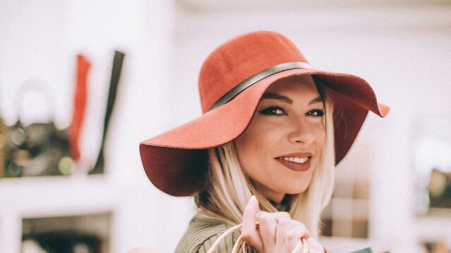 A woman wearing a wide-brimmed hat with a handbag over her shoulder smiling at the camera