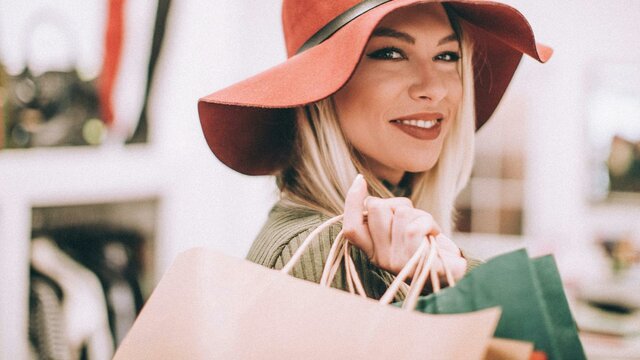 A woman wearing a wide-brimmed hat with a handbag over her shoulder smiling at the camera