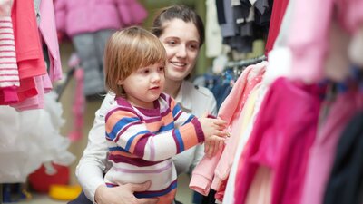 A small boy with a women touching clothes hanging on a rack at a market stall