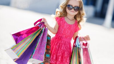 A young girl wearing sunglasses and holding shopping bags smiling for the camera at a market