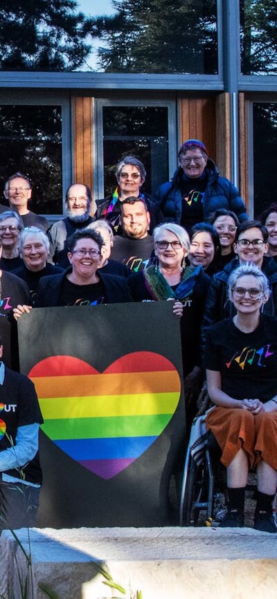 Picture of Canberra QWIRE people smiling and holding rainbow heart banners