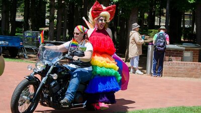 motorbike ridden by woman and drag queen passenger