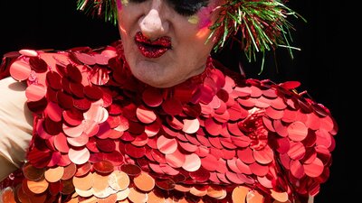 Drag Performer in brightly coloured costume and headress performing at Fair Day