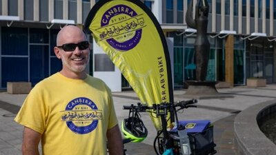 Man in yellow and purple branded t-shirt standing in front of yellow flag