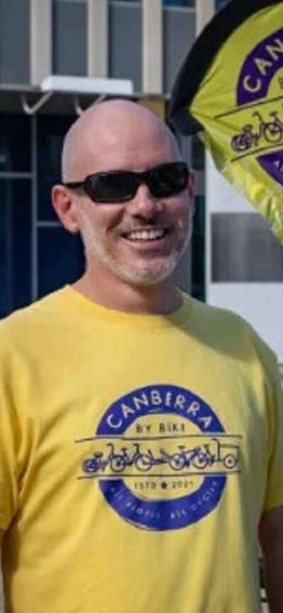 Man in yellow and purple branded t-shirt standing in front of yellow flag