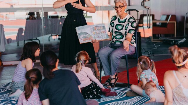 Community day in the Garden An Auslan interpreter standing next to a person reading a book to a group of children sitting down