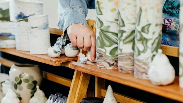 2025 Craft + Design Canberra Undercurrent Design Market at Gorman House A hand touching some ceramic vessels on a market stall display