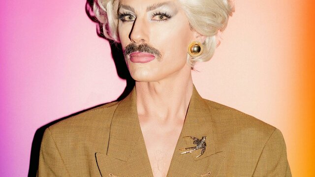 Venus Mantrap Drag artist man wearing a blonde wig and brown moustache