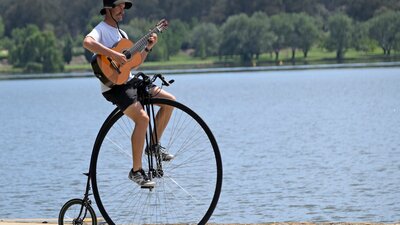 Simon playing a guitar while riding his penny-farthing