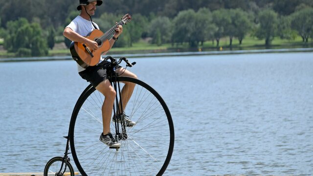 A penny-farthing Simon playing a guitar while riding his penny-farthing