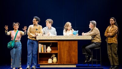 A group of people gather at a kitchen bench.