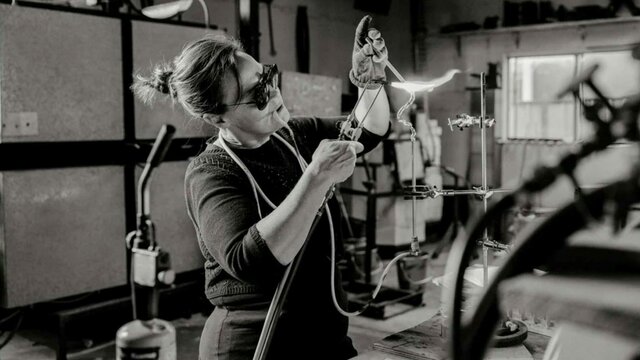 Harriet Schwarzrock in her studio A black and white photograph of the artist with a blow torch creating glass art