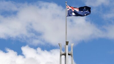 The Australian flag and top of the mast with blue sky and clouds in the background