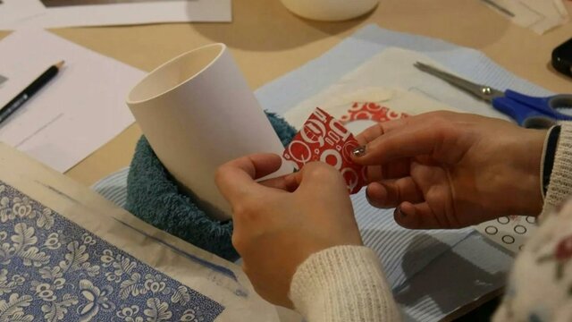 Ceramic Decal Decoration Workshop with Sarit Cohen, 2025 A close up shot of a pair of hands applying a red decal to a white ceramic cup