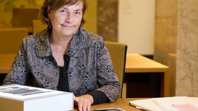 Dr Joy McCann A woman with brown hair is seated at a table, looking directly at the camera.