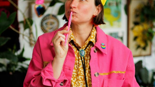 Georgina Chadderton A person with short dark hair and a yellow cap looks thoughtfully upward while holding a pink pen.
