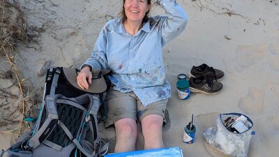 Sophie Baker Studio Shot Sophie Baker sitting on the beach (her studio for the day) with her canvas and paints