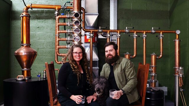 Renee & David (& Parker) are the founders of Everyday Legacy Craft Distillery Renee & David, distillery founders, sitting in front of their still with their dog Parker.