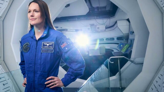 Katherine Bennell-Pegg A woman at a space station wearing a blue astronaut uniform