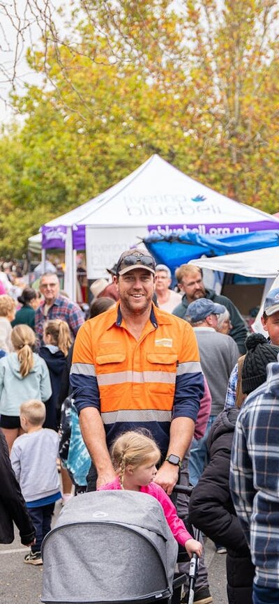 A crowd of people at street markets, main focus on a smiling  man pushing a pram.