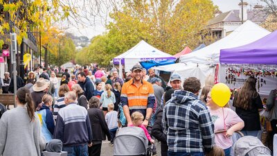 A crowd of people at street markets, main focus on a smiling  man pushing a pram.