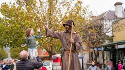 A child high is lifted to high five a stilt walker dressed as a wizard