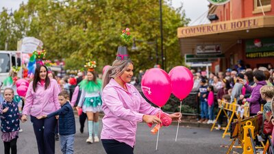 A woman in a pink shirt handing out pink balloons during a street parade.