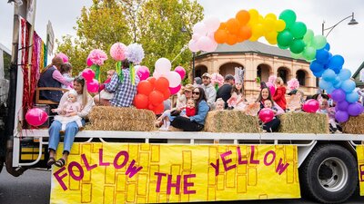 A group of children and adults on the back of a truck with the sign Follow the Yellow Brick Road.