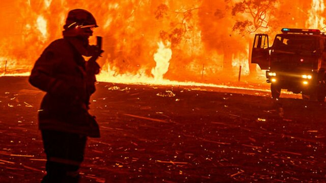 Fire Front (2022) Firefighters in the midst of burning bush with fire truck in the background