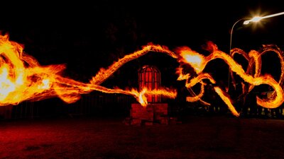 A long exposure photo of fire twirlers, with lines of flames pictured across a dark night background