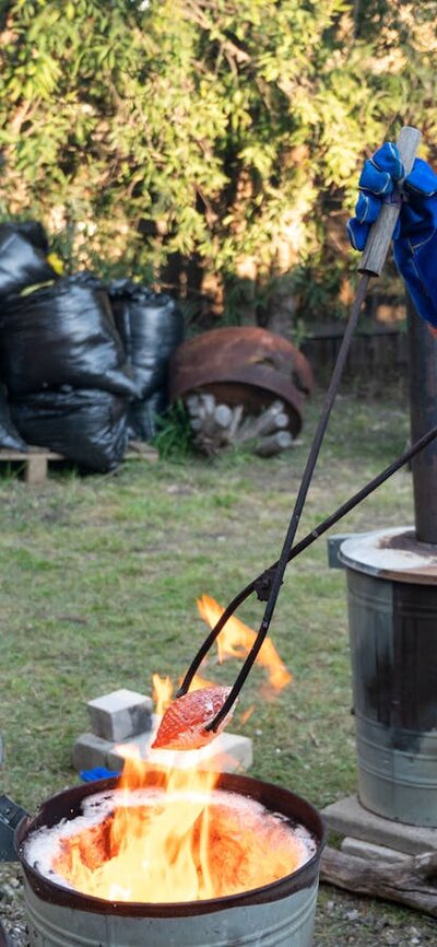 A volunteer used large tongs to pull out a red hot pottery piece from a flaming metal bin