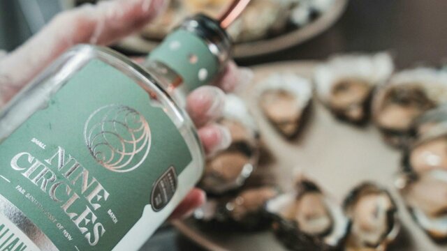 Gin + Oysters - a winning combo! Someone holding a bottle of gin in front of a plate of oysters