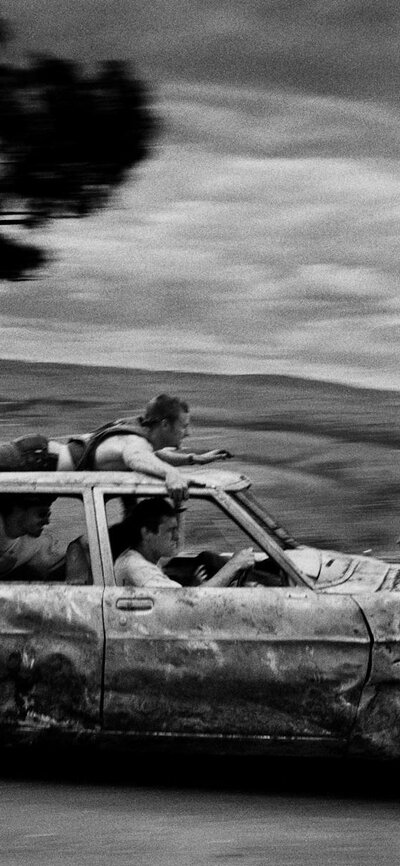 Trent Parke, Untitled #4 1998, from the series ‘Mount Pandemonium, Bathurst, NSW’, National Gallery black & white image of a banged-up car speeding past with passengers and one man on the car roof