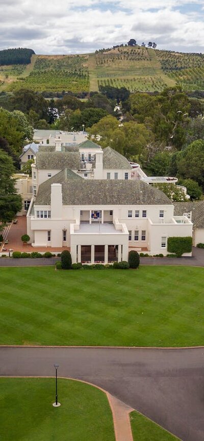 Lawn leading into a large white house surrounded by trees