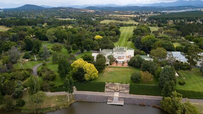 An aerial photo showing water, lawn, a large white house and surrounding trees