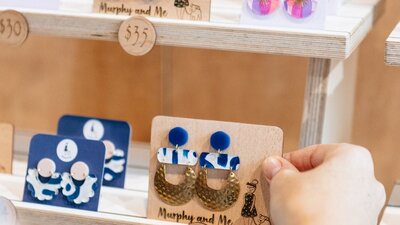 A person picking up blue, white and gold Murphy and Me earrings at the Handmade Market