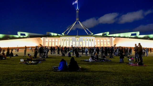 Night-time view of Australian Parliament House, brightly lit against a dark blue sky.