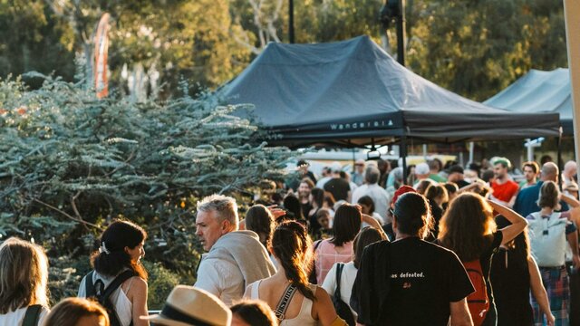 Festivals at National Museum of Australia A bustling crowd outdoors at sunset. Tents and trees are visible,