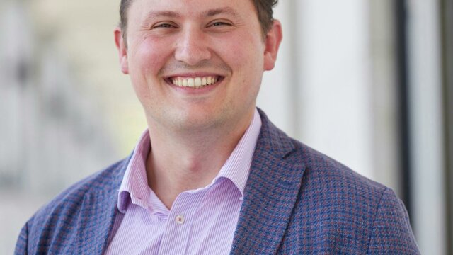 Dr Samuel White A man wearing a button down shirt and blue blazer while smiling at the camera