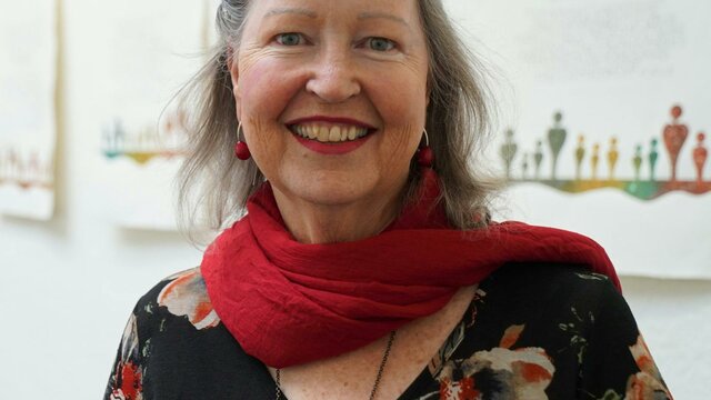 Gemma Black A smiling woman with gray hair wearing a red scarf over a dark floral top.