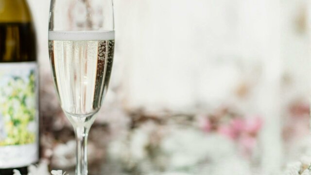 Glass of sparkling wine next to bottle with a mirror as a table and floral arrangements