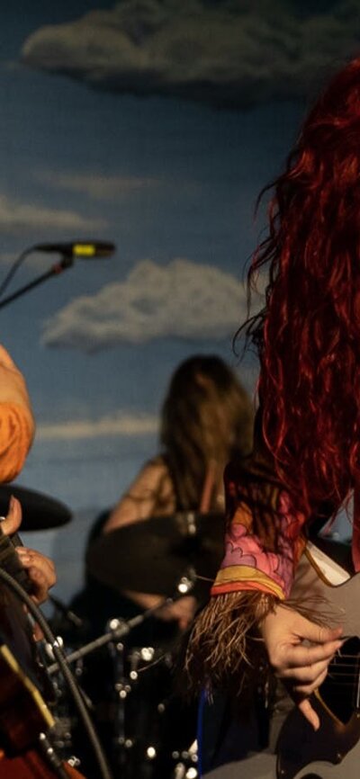 Little Quirks performing on stage 2 young woman dressed in fun outfits play guitars and sing against a sky blue backdrop