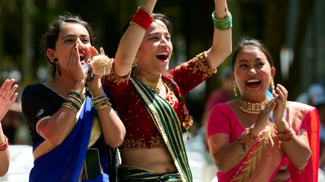 Celebrate with us at the 2024 National Multicultural Festival! Three women in cultural dress clap for the festival parade performers