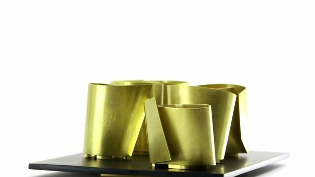 Radka Passianova | Circles Not Allowed 2026 A collection of brass metal vessels with sharp angles sits on a platter against a white background
