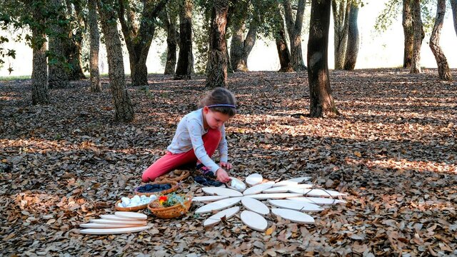 A young girl plays with wooden mandala shapes on a leafy forest floor